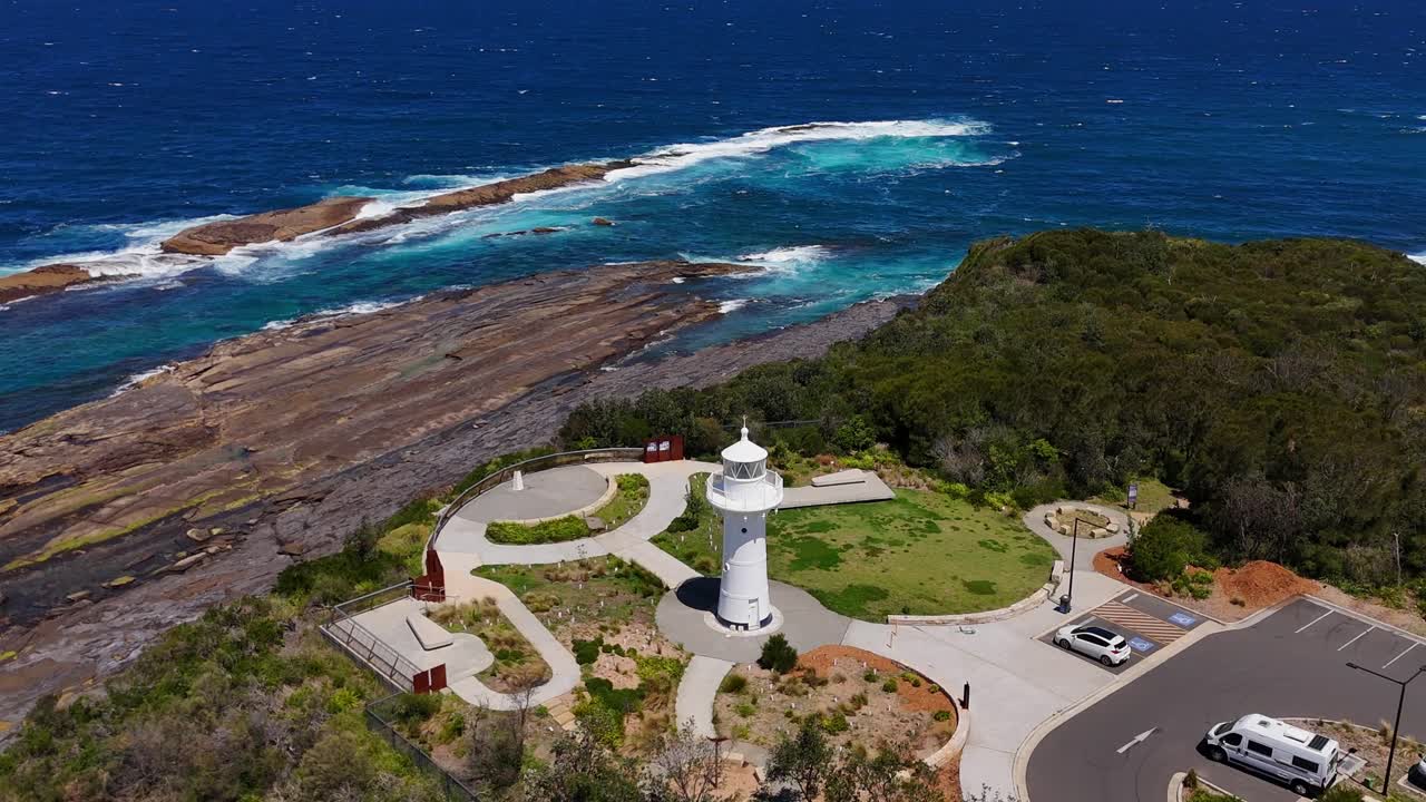 Aerial slow orbit of Warden Head Lighthouse perched beside cliffs with rolling surf along the shore, Australia