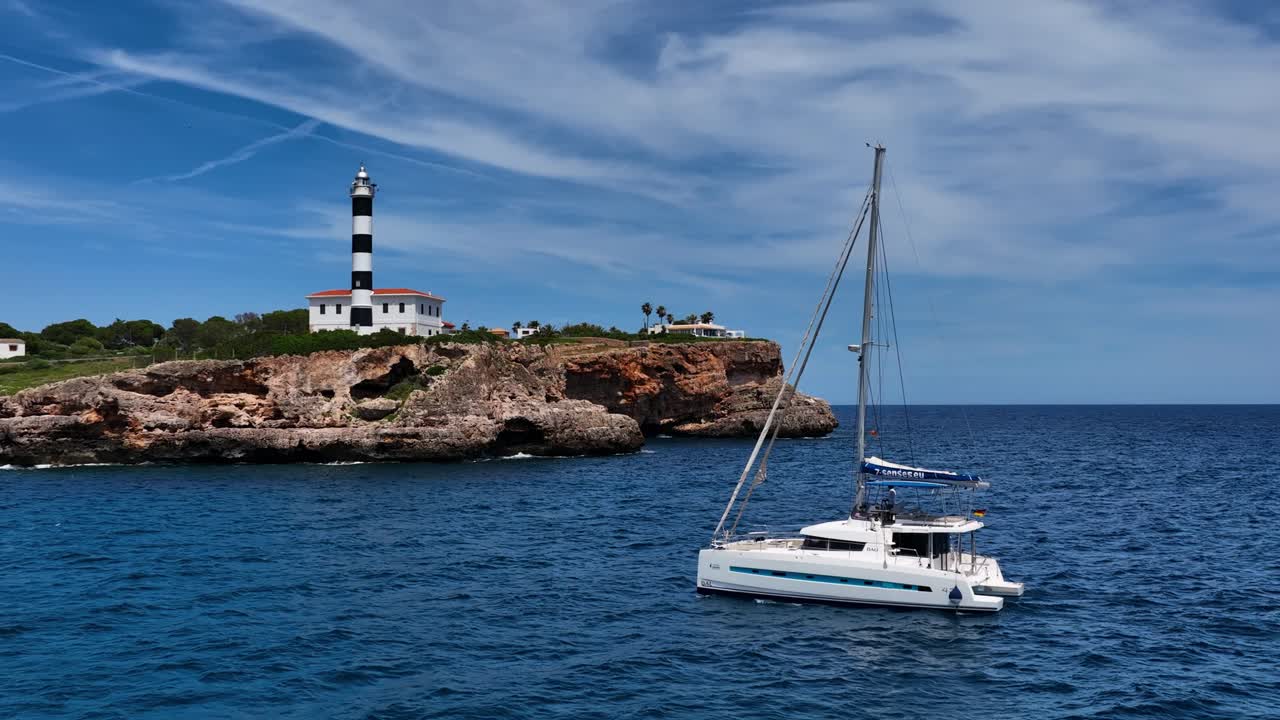 Filmato aereo con drone di un catamarano a vela che supera scogliere e un faro lungo la costa di Maiorca