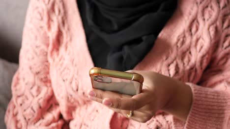 mujer usando un teléfono inteligente mientras lleva un hijab y un suéter rosa