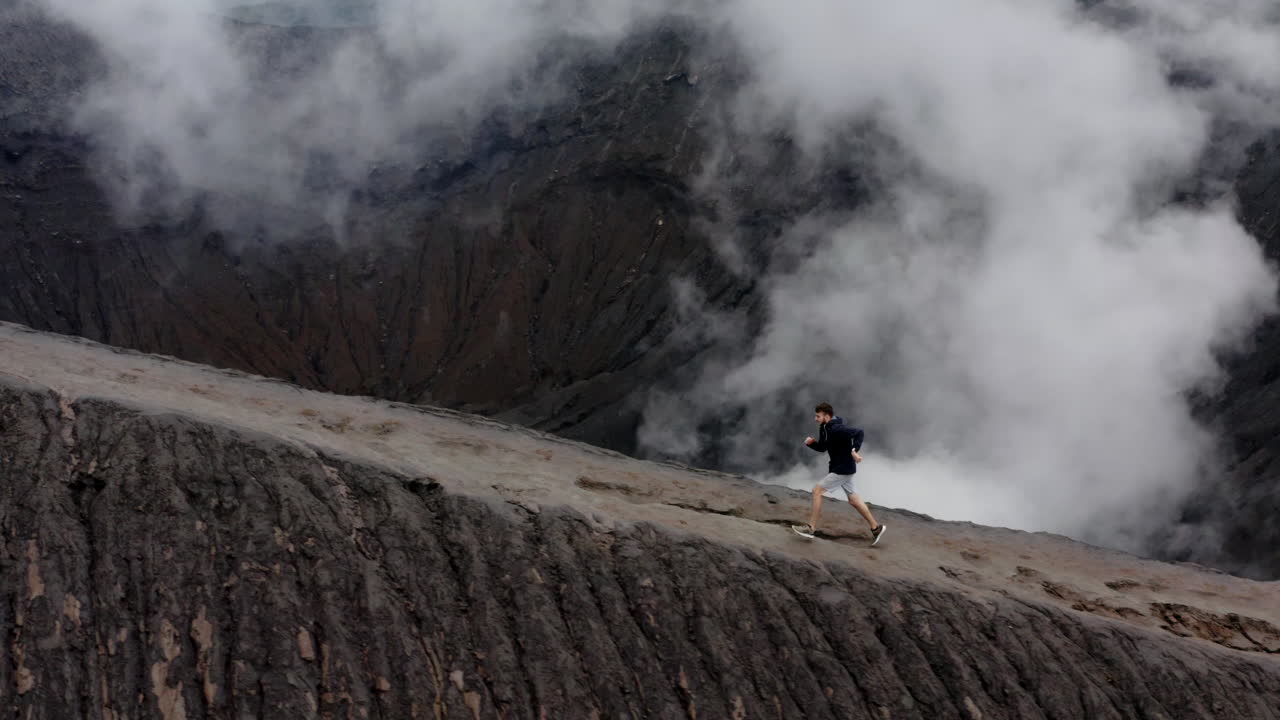 Aerial orbit tracking active young man running on Volcano