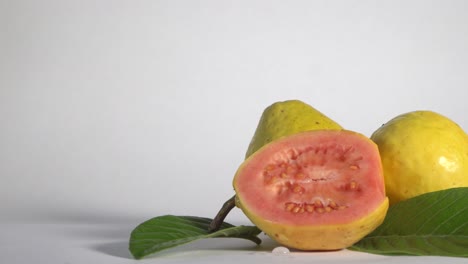 fruta de guayaba entera y media aislada en fondo blanco, alejamiento lento