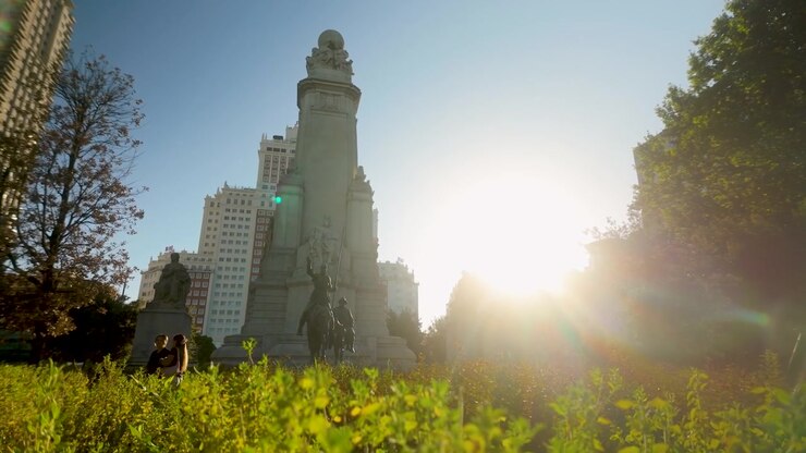 Un'inquadratura dal basso del monumento a Cervantes a Madrid, Spagna, con la statua di Don Chisciotte, un forte bagliore di luce solare e gli edifici della città. Utile per documentari di viaggio e storici.