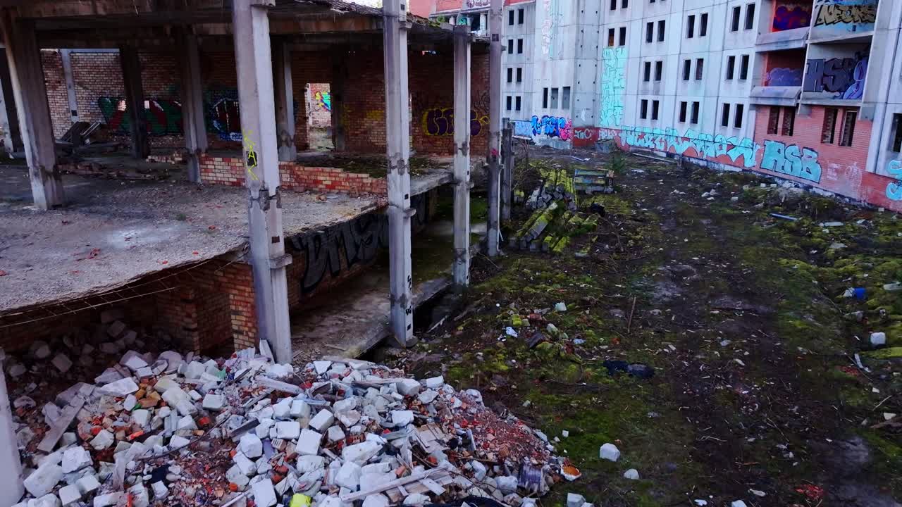 Empty shell of concrete buildings reclaimed by moss, graffiti amid forest edges