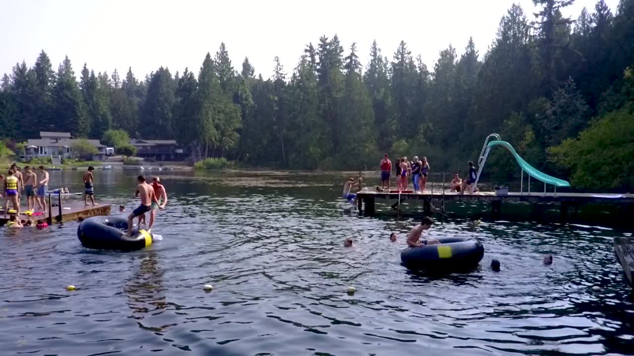 People Playing And Having Fun On The Calm Lake In Washington, USA With Lush Pine Trees In The Background - Slow Motion