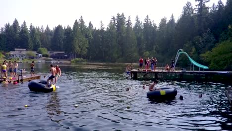 people playing and having fun on the calm lake in washington, usa with lush pine trees in the background - slow motion