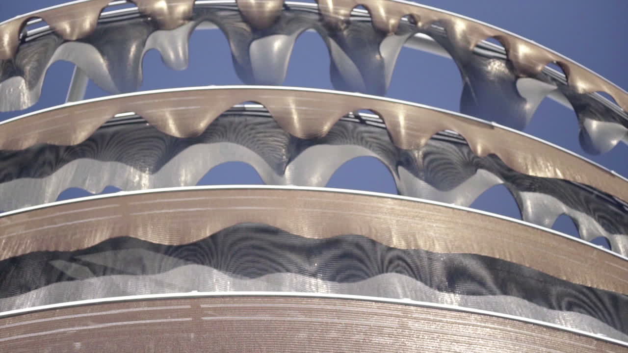 Close-up of a modern architectural or art structure featuring undulating metallic mesh patterns against a blue sky