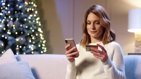 primer plano retrato de mujer hermosa positiva feliz comprando en internet regalos de navidad pagando con tarjeta de crédito usando el teléfono celular en una acogedora casa decorada