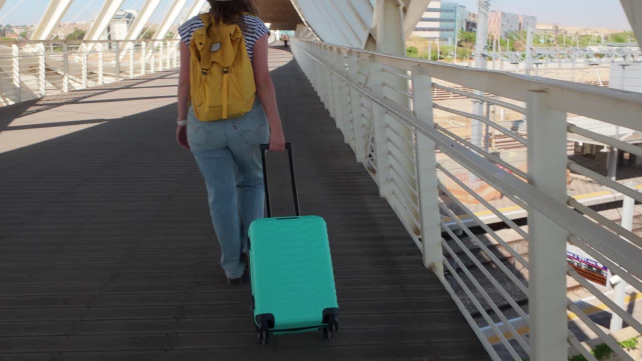 A woman is walking with a green suitcase on a bridge. The bridge is long and has a lot of space