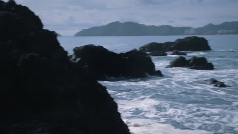 waves crashing against the large black rocks by the coast