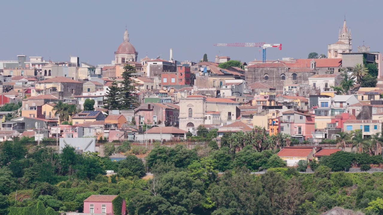 Ampia veduta aerea panoramica della SS114, una strada panoramica lungo scogliere di lava basaltica nera ed edifici colorati con una vista dello skyline della colorata Acireale, vicino a Catania, Sicilia, Italia, sulle colline dell'Etna.