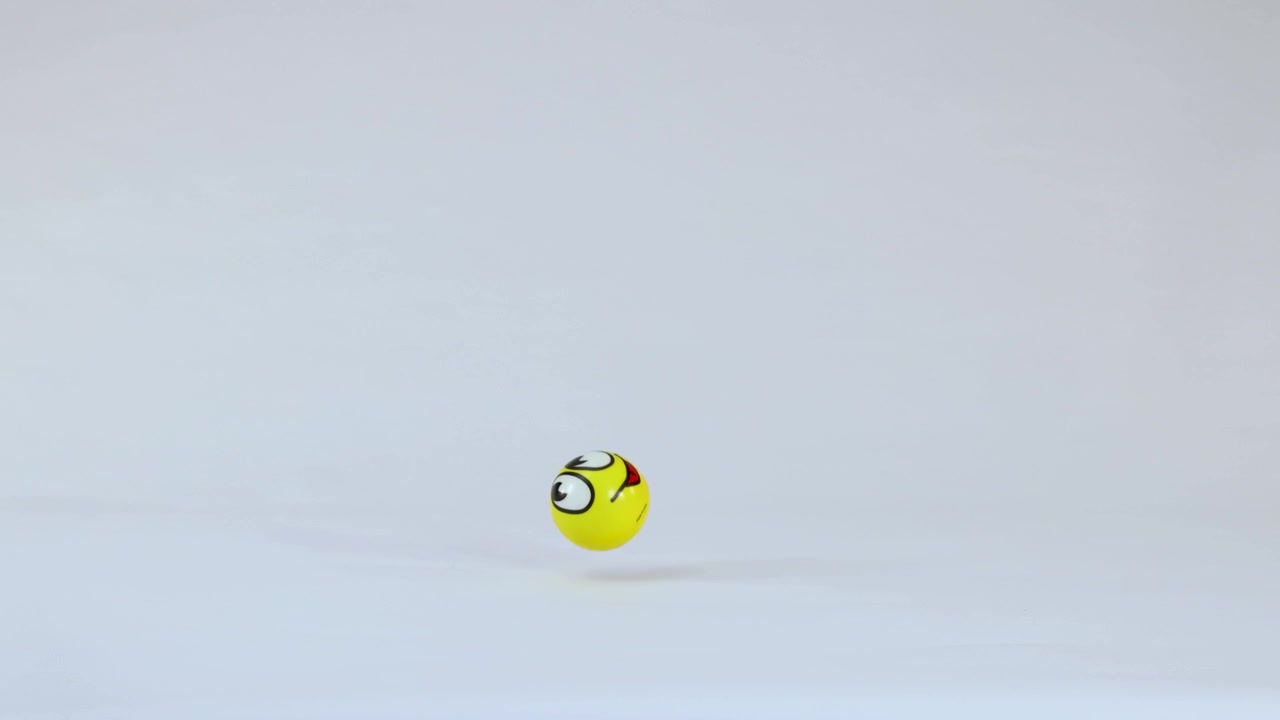 A yellow ball with a smiling face bounces and rolls across a white studio floor