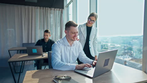 business lady prizing her colleague sitting at desk tapping by his shoulder. young team working in a sunlit modern office.