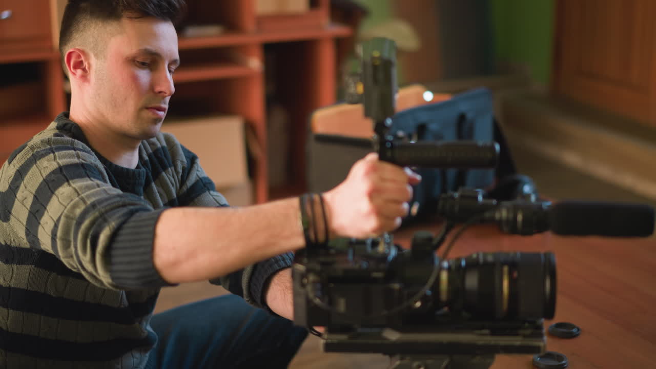 TV technician adjusting camera equipment on set. Person is holding camera rig with lens and microphone, working with tools to ensure setup is functioning. Indoor studio environment