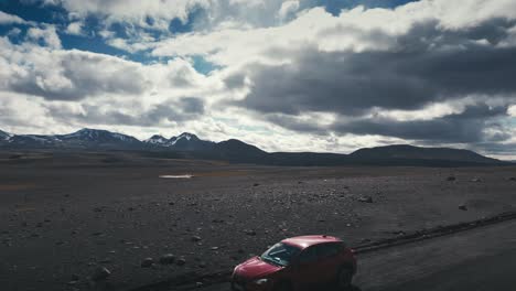 gorgeous drone aerial shot of a single passenger car traveling on a desert road with mountains in the background