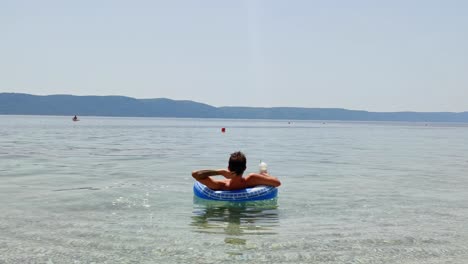 Static-shot-of-guy-on-inflatable-tube-in-the-sea-with-drink-relaxing-in-the-sun