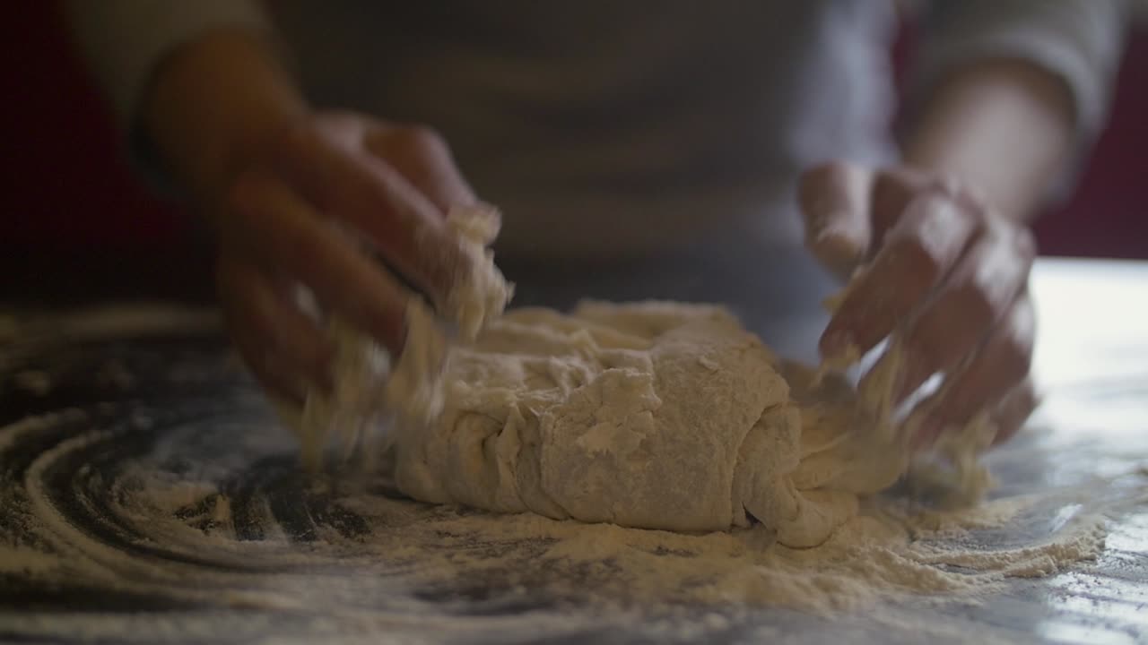 Mani di donna che preparano l'impasto della pizza su un tavolo di marmo.