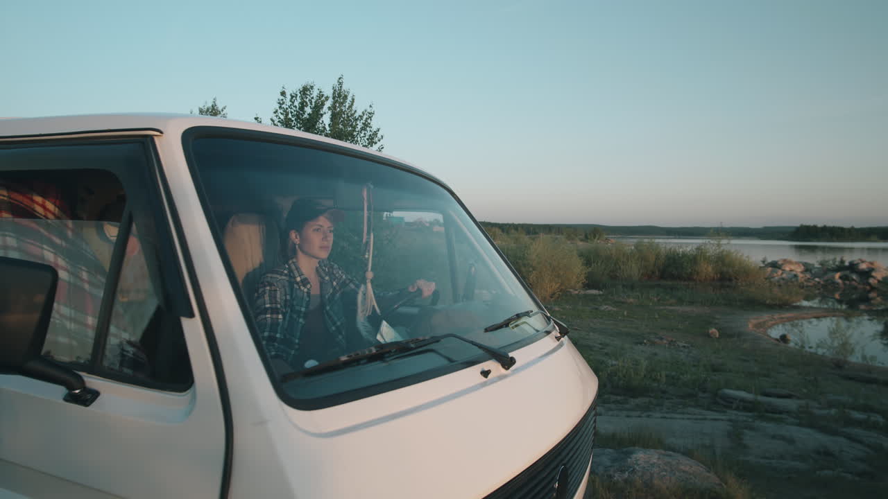Donna che scende dal furgone e guarda il tramonto dalla riva del lago