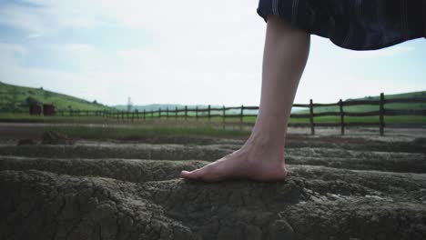 low-angle close-up of a woman's bare feet carefully walking across the cracked, and dry terrain of a mud volcano. the scene evokes a sense of exploration and connection to a rare natural wonder.