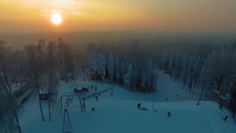 Forward-aerial-view-of-a-skiing-terrain-park-surrounded-by-fir-tree-forest-at-sunset