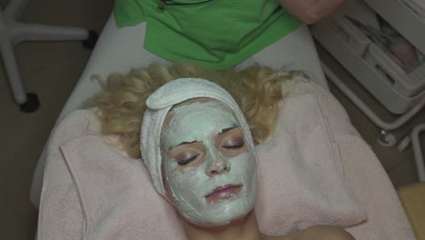 woman with facial mask on skin care treatment in spa salon, dermatology and anti aging concept, high angle view