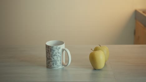 static shot of a cup of coffee and two green apples on kitchen table