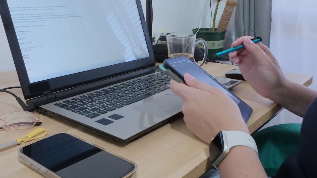 Detailed close-up of hands using a tablet with a stylus, alongside a laptop.