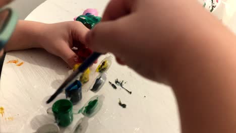 close-up. the boy is playing with the paint at the table. he wipes the brush into a white handkerchief. boy with glass