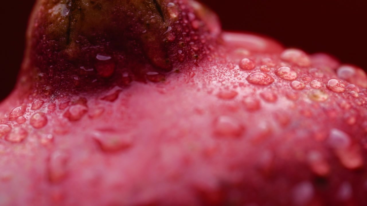 Frutto di melograno rosso coperto di goccioline d'acqua su sfondo rosso