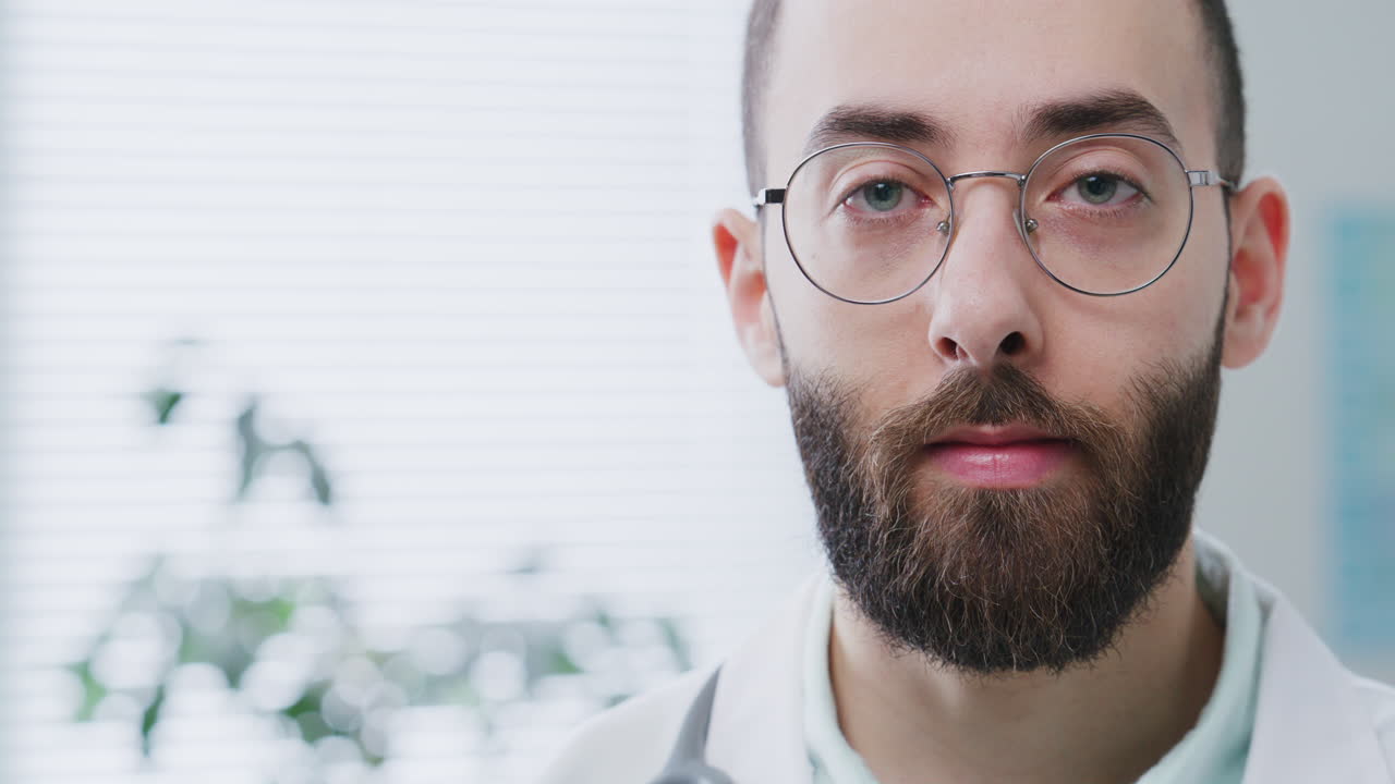 Ritratto di medico uomo barbuto con gli occhiali che guarda la telecamera in uno studio medico