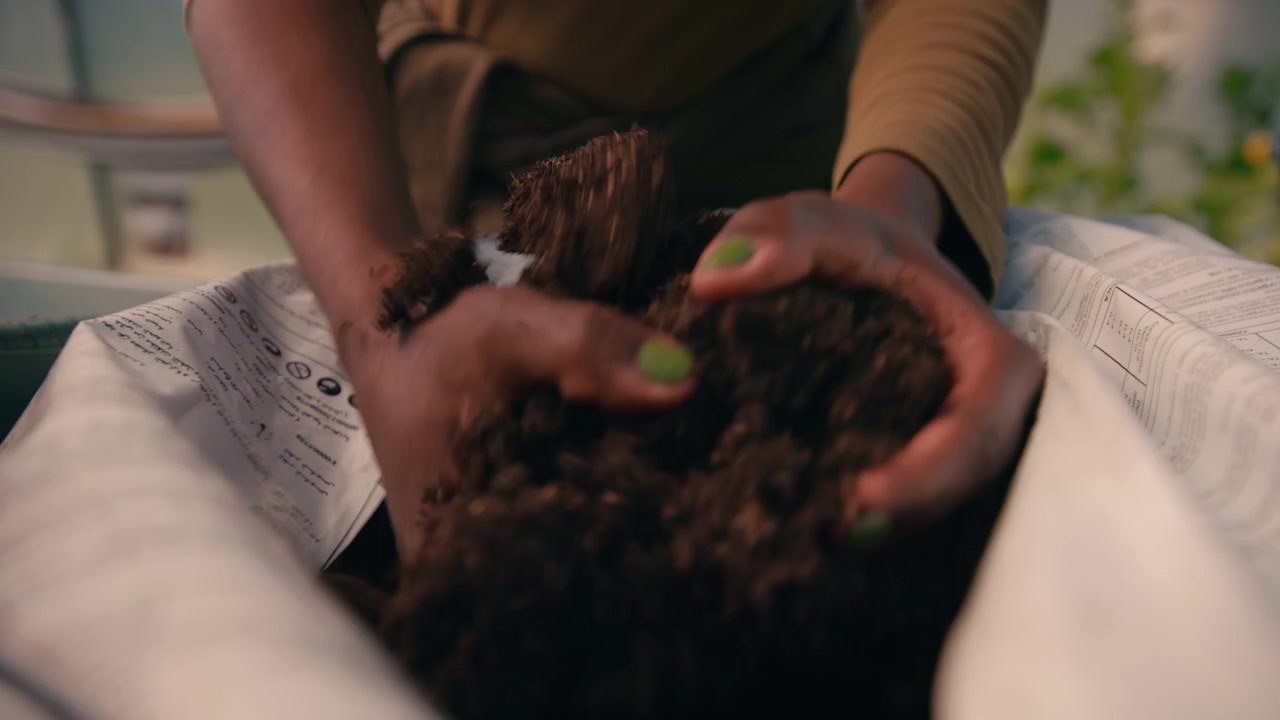 Close-up of hands scooping compost from a bag into a wheelbarrow inside a polytunnel.