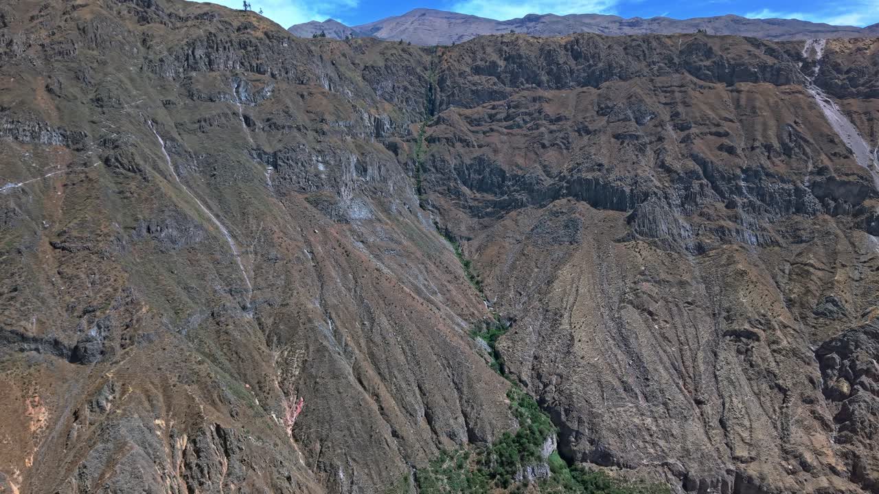 La ripresa inversa di un drone rivela la ristrettezza della vivace striscia verdeggiante di vita nel Canyon del Colca; la telecamera si allontana e le infinite e brulle scogliere dominano l'inquadratura, sottolineando la speranza, la sopravvivenza e la fragilità in un paesaggio estremo.