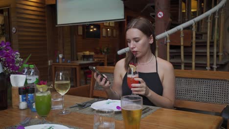 a static shot of a young woman is sitting alone in a restaurant on a coffee break, surfing phone, and having a juice for drink