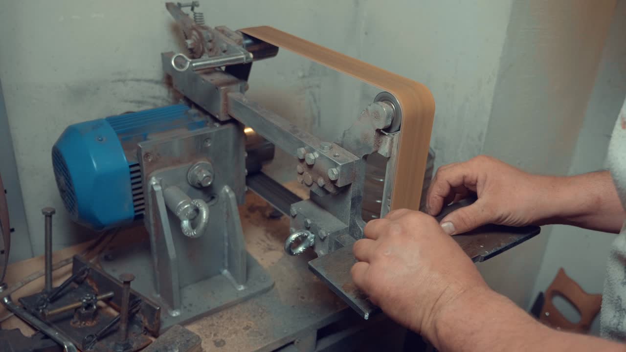 artesano afilando la hoja del cuchillo en un torno de molienda profesional en el taller. fabricación de cuchillos diy