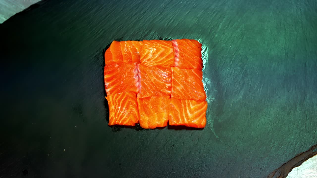 Un sashimi a base di filetto di salmone crudo viene servito su un piatto di ardesia decorato con erbe aromatiche