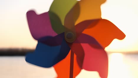 rotate plastic pinwheel rotate with a blowing wind stands on sand by the sea against the smooth surface of the sea and a bright pink sunset. toy mill on the beach. large disk of the sun. copy space