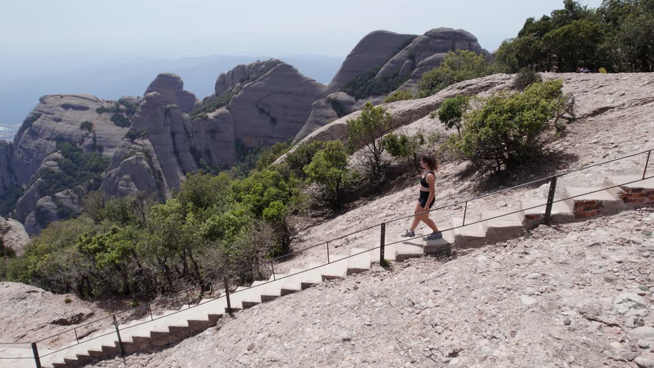 mujer joven caminando en el parque nacional de la montaña de montserrat, barcelona, españa, un avión no tripulado la sigue, concepto de bienestar y naturaleza