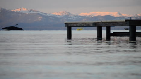 calm waves crash against pier in lake tahoe with snowy mountains in the background