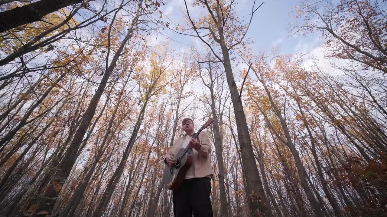 Parkta sarı yapraklarla sonbahar fonunda gitar çalan adam.