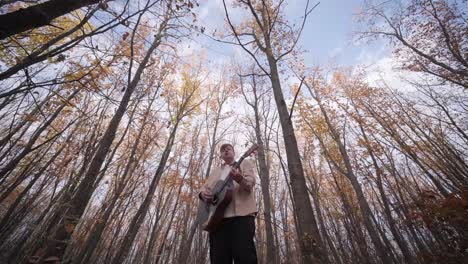 guy playing by the guitar in autumn background with yellow leaves in the park
