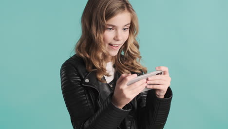 una adolescente caucásica con chaqueta de cuero jugando juegos en línea en su teléfono inteligente.