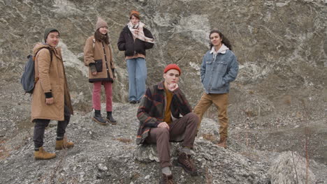 group of teenage friends dressed in winter clothes posing looking at camera, sitting and standing on the mountain