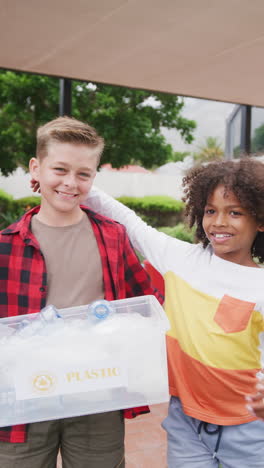 vertical video of two happy diverse boys collecting recycling, embracing in schoolyard, copy space
