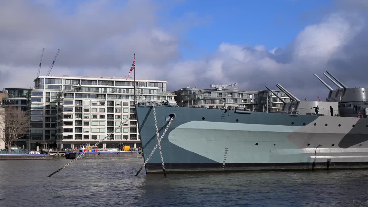 Una prospettiva dalla Southbank che mostra lo scafo massiccio in acciaio grigio e i ponti superiori della storica nave da guerra HMS Belfast ormeggiata sul fiume Tamigi.
