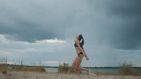 slender beach volleyball player woman is serving ball on sand court full length shot against cloudy sky