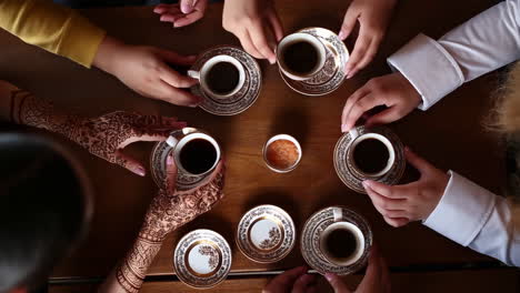 overhead view of multiple people gathered around a table with coffee cups, one person with henna-decorated hands