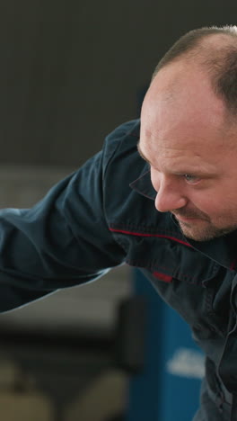 mechanic in blue uniform using torchlight to inspect car tire in auto repair shop, focusing closely with blue lift in background, ensuring safety and maintenance in professional automotive workshop