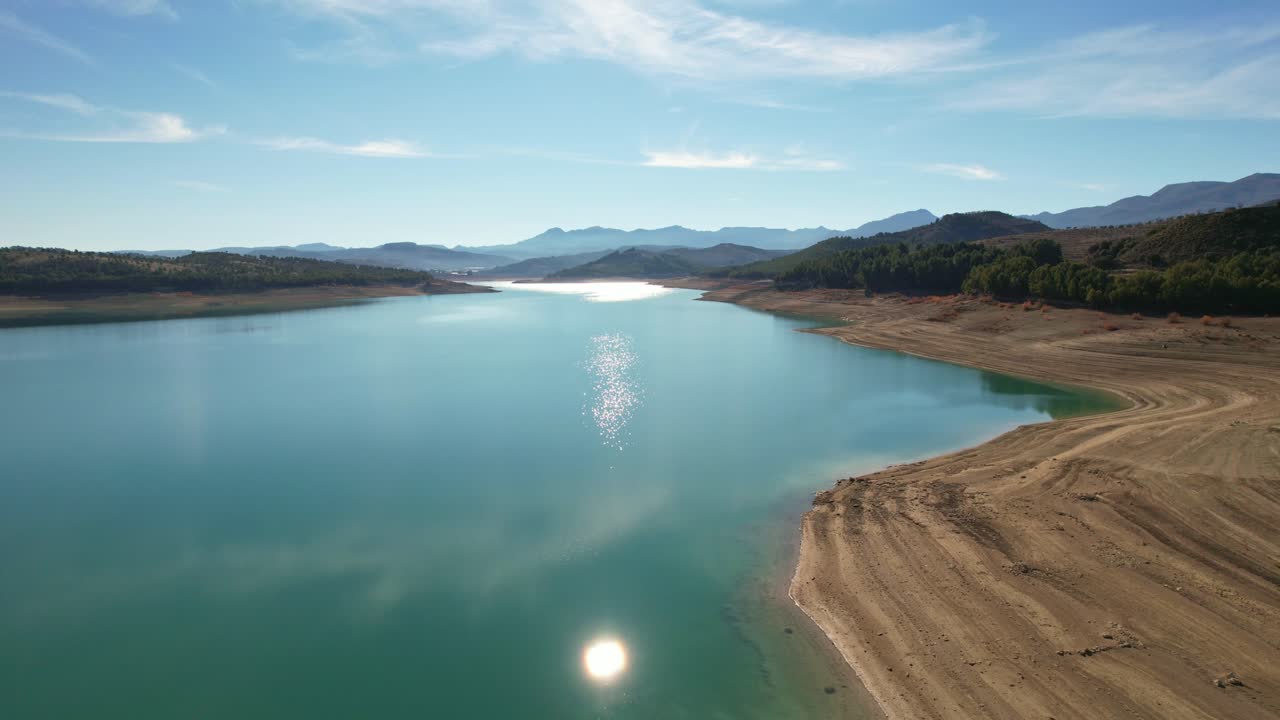 Reflection of the sun on calm lake waters. Sky and clouds reflected in the lake waters. Mirror effect. Aerial view of a beautiful lake surrounded by mountains