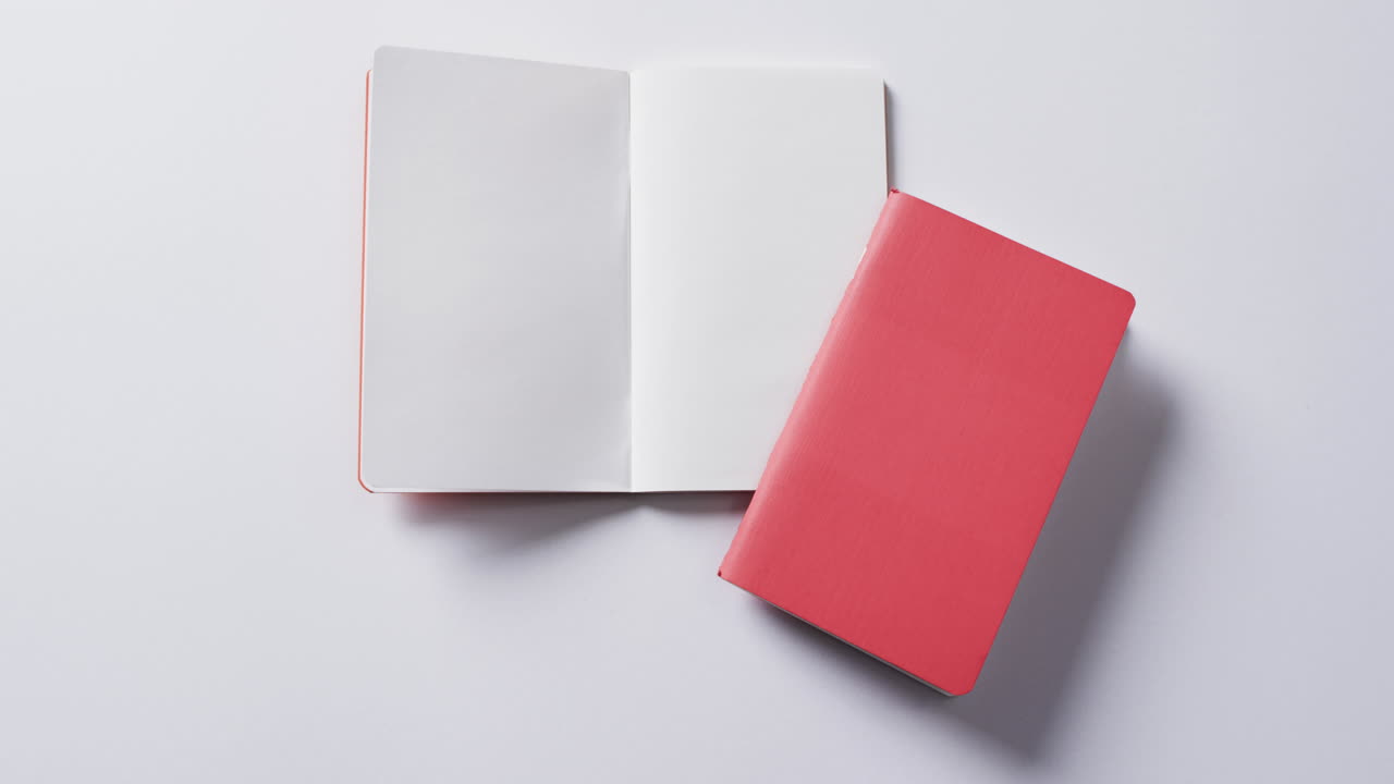 Close up of closed red book and open blank book with copy space on white background in slow motion