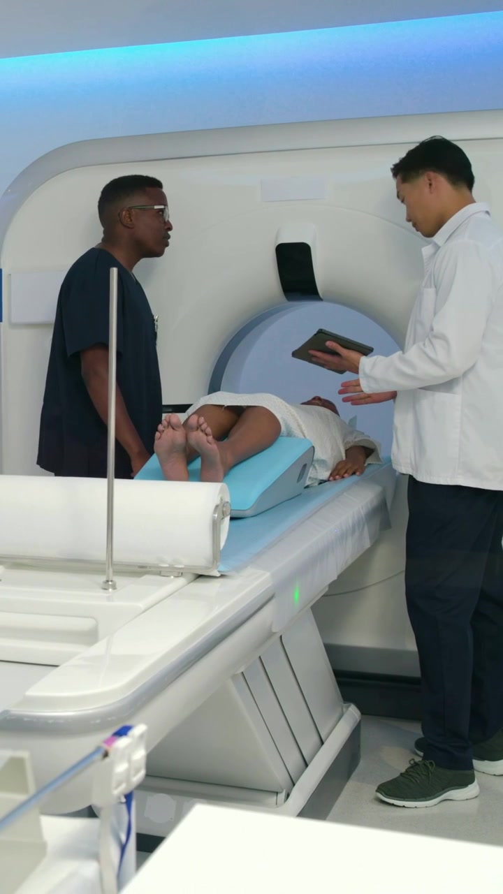 Video verticale: Tecnico in camice da laboratorio che tocca un tablet e si inserisce nell'apertura della macchina per la scansione, mentre un altro tecnico controlla il cuneo.