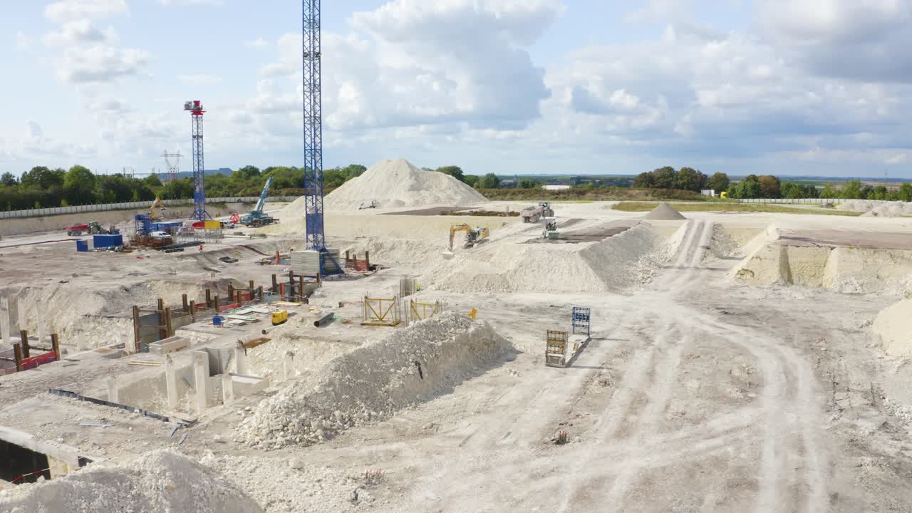 drone aéreo hacia adelante disparo en movimiento volando sobre jcb y cavando tierra y depositando en el camión en un sitio de construcción en un día soleado